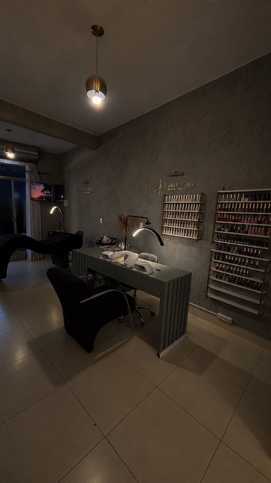 Vista do studio com iluminação dourada, bancada e prateleiras de esmaltes